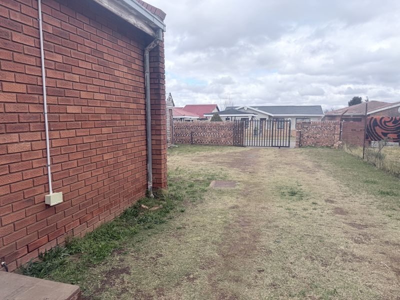 A view of the rear yard featuring a brick exterior wall, a metal gate, and a grassed area.