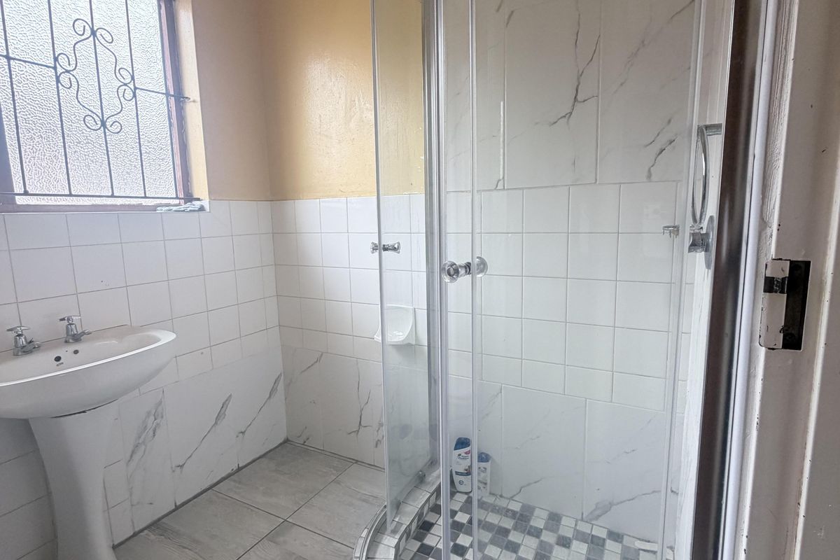 A functional bathroom featuring a pedestal basin, a corner shower enclosure with glass doors, and tiled finishes throughout.