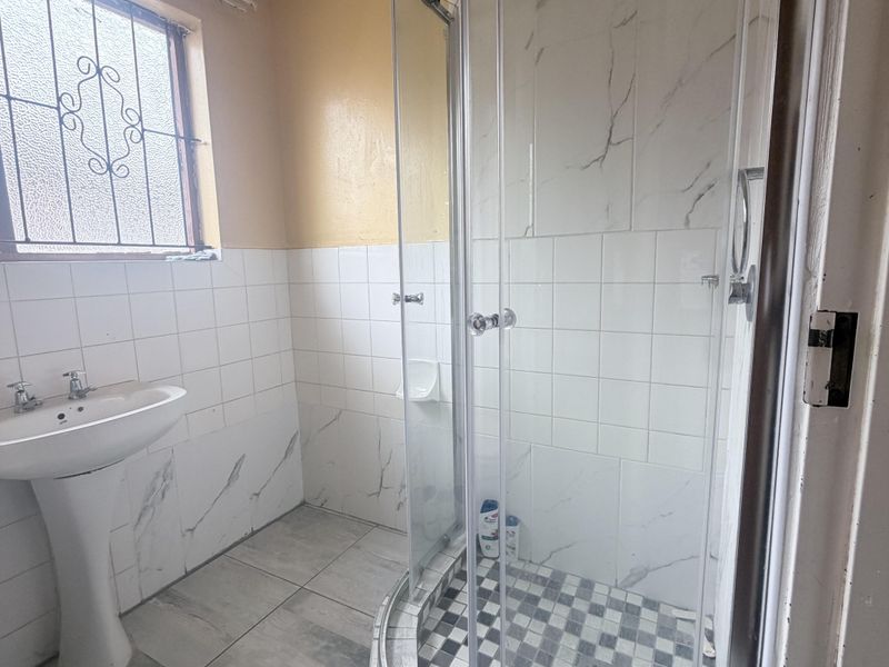 A functional bathroom featuring a pedestal basin, a corner shower enclosure with glass doors, and tiled finishes throughout.
