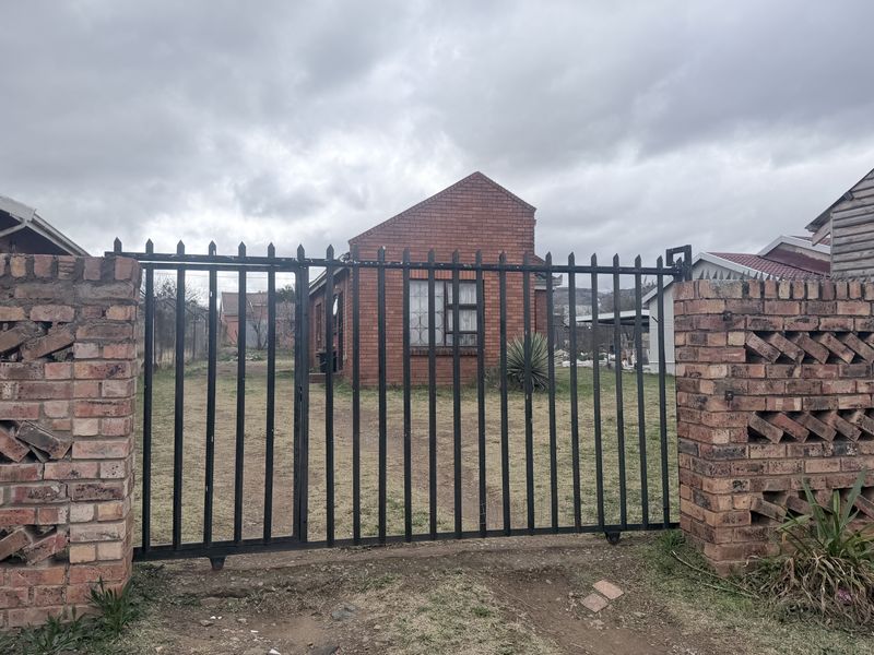 Front view of a face brick house featuring a secure metal gate and brick perimeter walling.