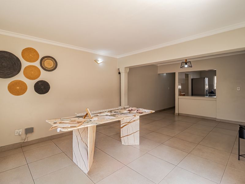 Spacious open-plan living and dining area featuring neutral tiled flooring, decorative coving, and a convenient pass-through window connecting to the kitchen.