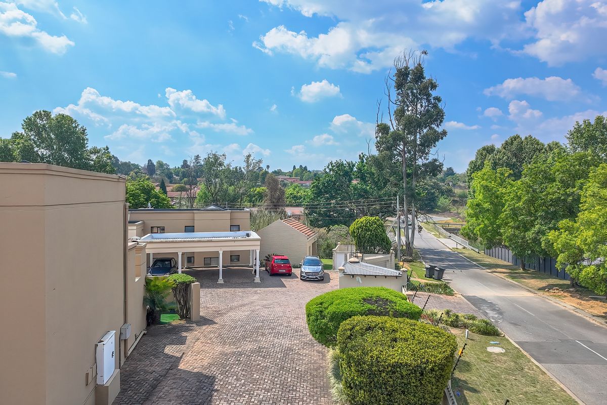An elevated view of the property exterior, featuring a paved driveway, carport, and well-maintained landscaped garden area.