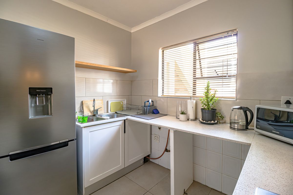A functional kitchen area featuring built-in cabinetry, a stainless steel sink, tiled backsplash, and a window with blinds, providing a clean and practical workspace.