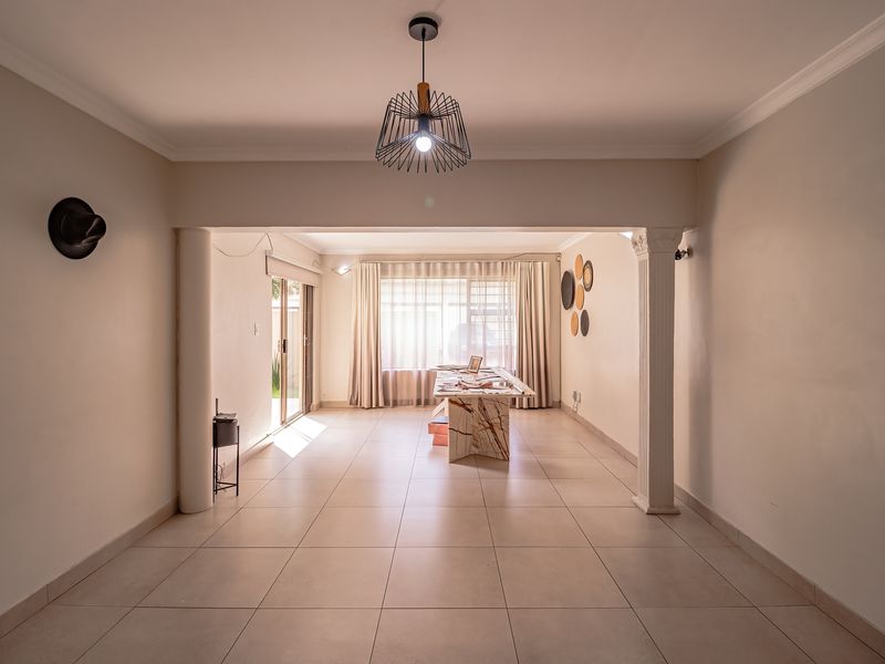 Spacious open-plan living area featuring neutral tiled flooring, decorative columns, and abundant natural light through large windows and sliding glass doors.
