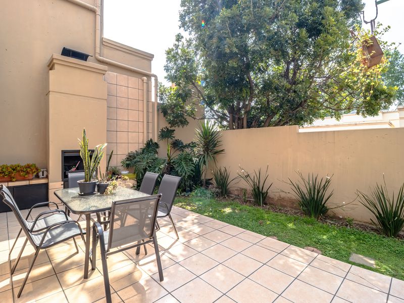 Private patio area featuring a built-in braai, tiled flooring, and a small garden space enclosed by a boundary wall.