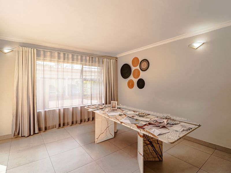 A bright and spacious living area featuring neutral tiled flooring, cove cornicing, and wall-mounted lighting, offering a clean canvas for interior design.