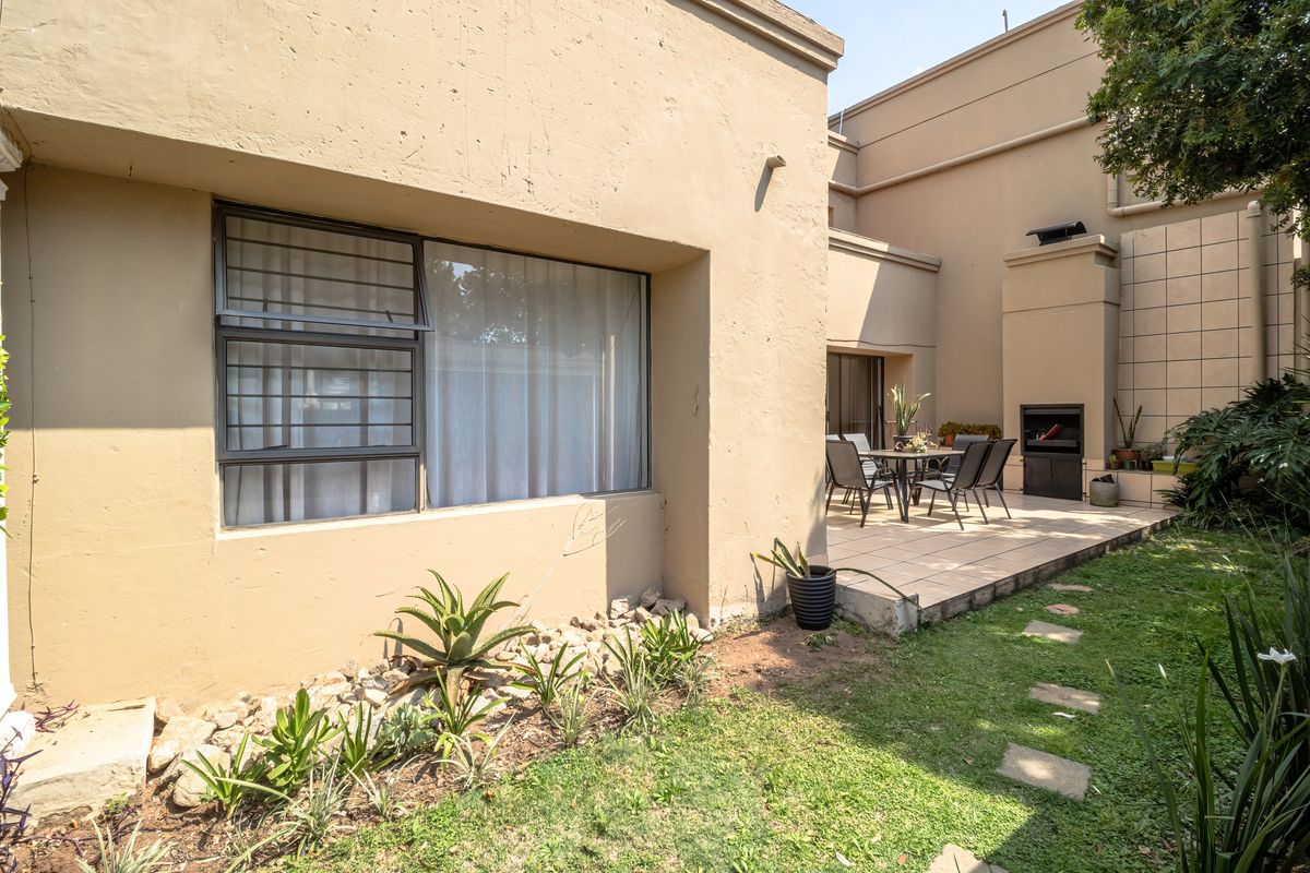 Rear exterior view featuring a tiled patio area with a built-in braai, adjacent to a small garden with paved stepping stones.