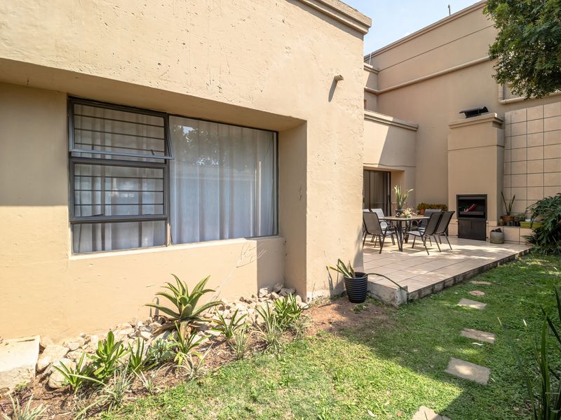 Rear exterior view featuring a tiled patio area with a built-in braai, adjacent to a small garden with paved stepping stones.