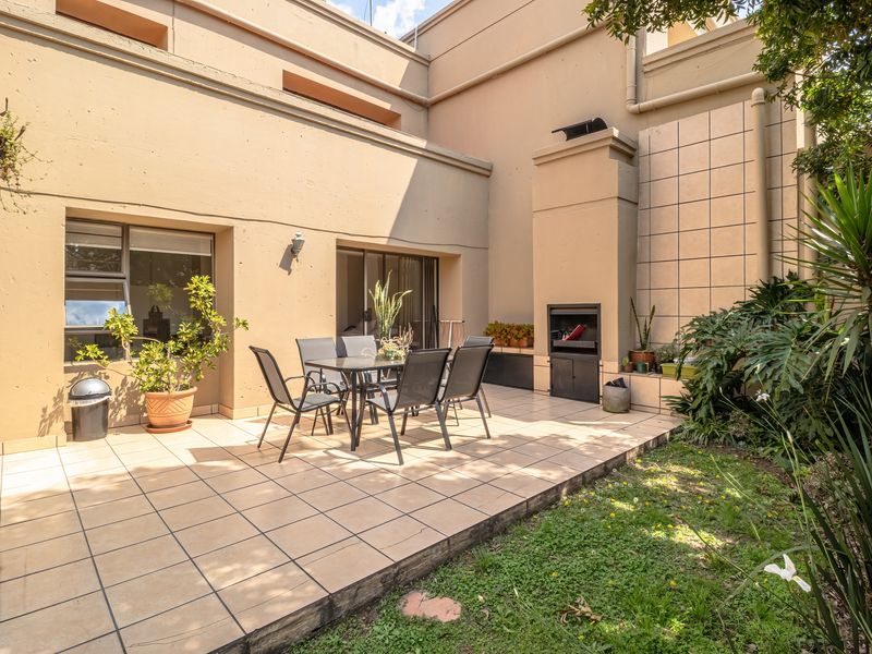 A private outdoor patio area featuring tiled flooring, a built-in braai, and direct access to the interior through sliding glass doors.