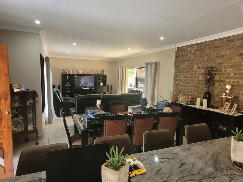 Spacious open-plan living and dining area featuring an exposed brick feature wall, recessed lighting, and a large stone-topped kitchen island.