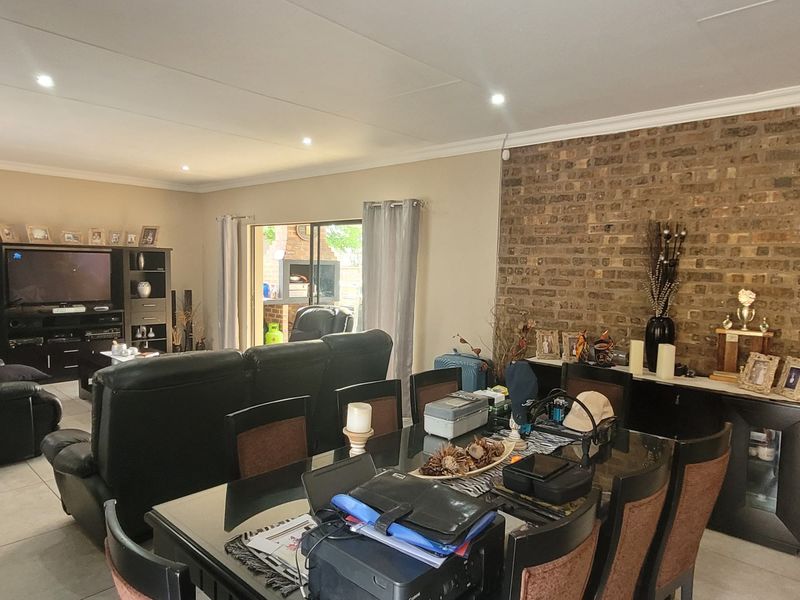 Spacious open-plan living and dining area featuring a prominent exposed brick feature wall, tiled flooring, and recessed lighting with access to the patio.
