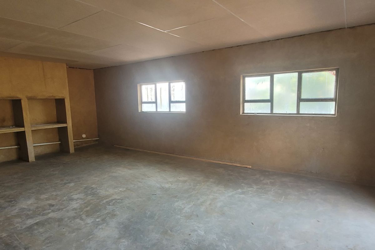 An unfinished living area featuring raw plaster walls, exposed concrete flooring, and built-in shelving, offering a blank canvas for renovation and custom finishes.