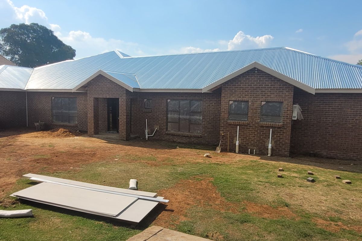 Rear view of a newly constructed face brick house featuring a corrugated metal roof and unfinished landscaping.