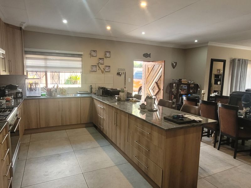 Spacious open-plan kitchen and dining area featuring modern wood-finish cabinetry, stone countertops, integrated appliances, and large format floor tiles.