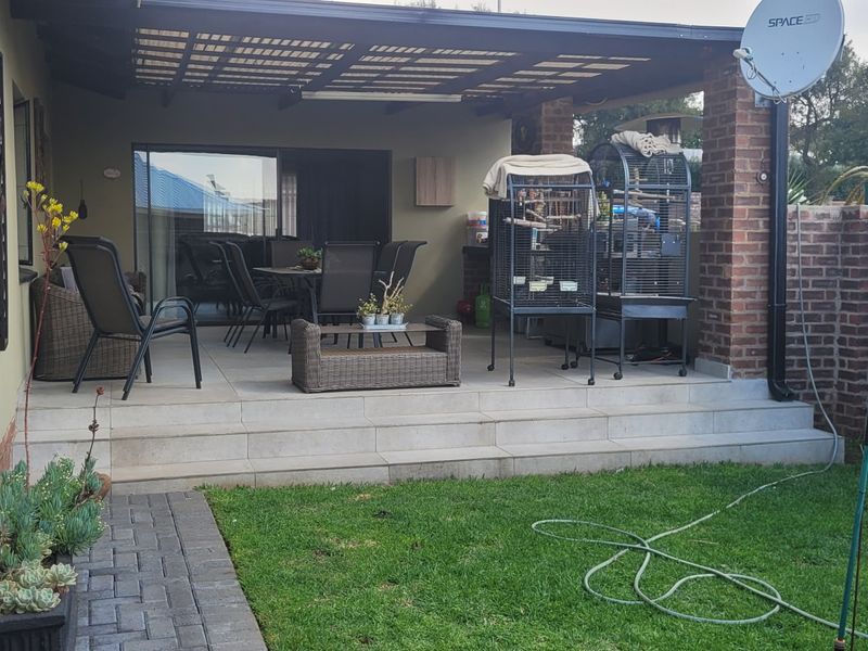 A covered outdoor patio area featuring tiled flooring, brick pillars, and direct access to the home through sliding glass doors, overlooking a small garden.