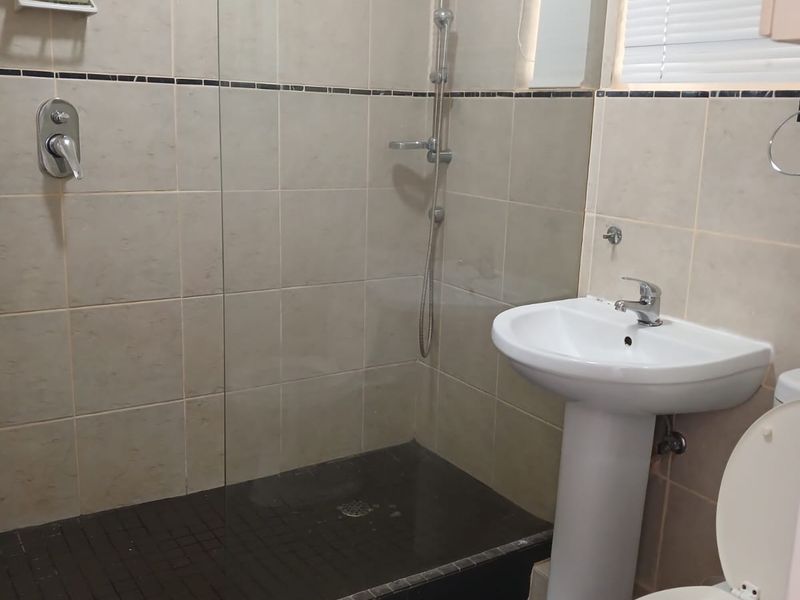 A functional bathroom featuring a walk-in shower with glass screen, pedestal basin, and tiled finishes throughout.