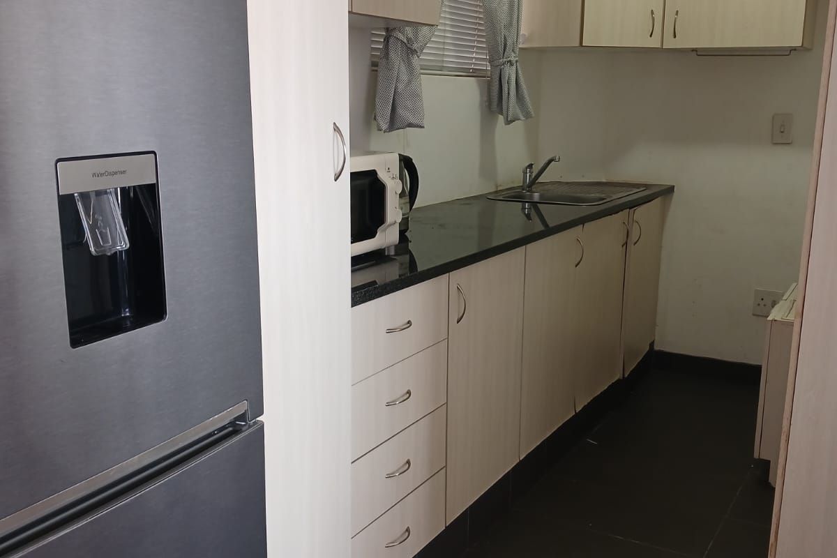 A compact kitchen featuring light-toned laminate cabinetry, dark granite countertops, a stainless steel sink, and dark floor tiles.