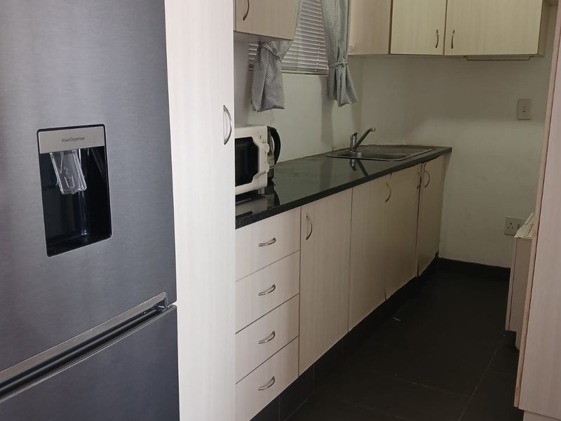 A compact kitchen featuring light-toned laminate cabinetry, dark granite countertops, a stainless steel sink, and dark floor tiles.