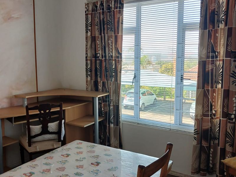 A bedroom featuring a ceiling fan, ventilation grilles, and large windows with venetian blinds, offering natural light and a view of the exterior.