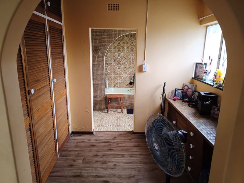 Bedroom featuring built-in wooden cupboards, laminate flooring, and an adjoining bathroom with decorative tiled finishes and a built-in bathtub.