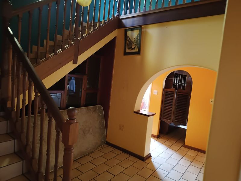 Entrance hallway featuring a wooden staircase with balustrade, tiled flooring, and an arched doorway leading to adjacent living spaces.