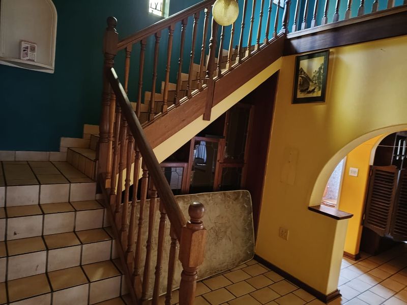 A traditional hallway featuring a wooden staircase with a balustrade, tiled flooring, and an arched entryway leading to adjacent living spaces.