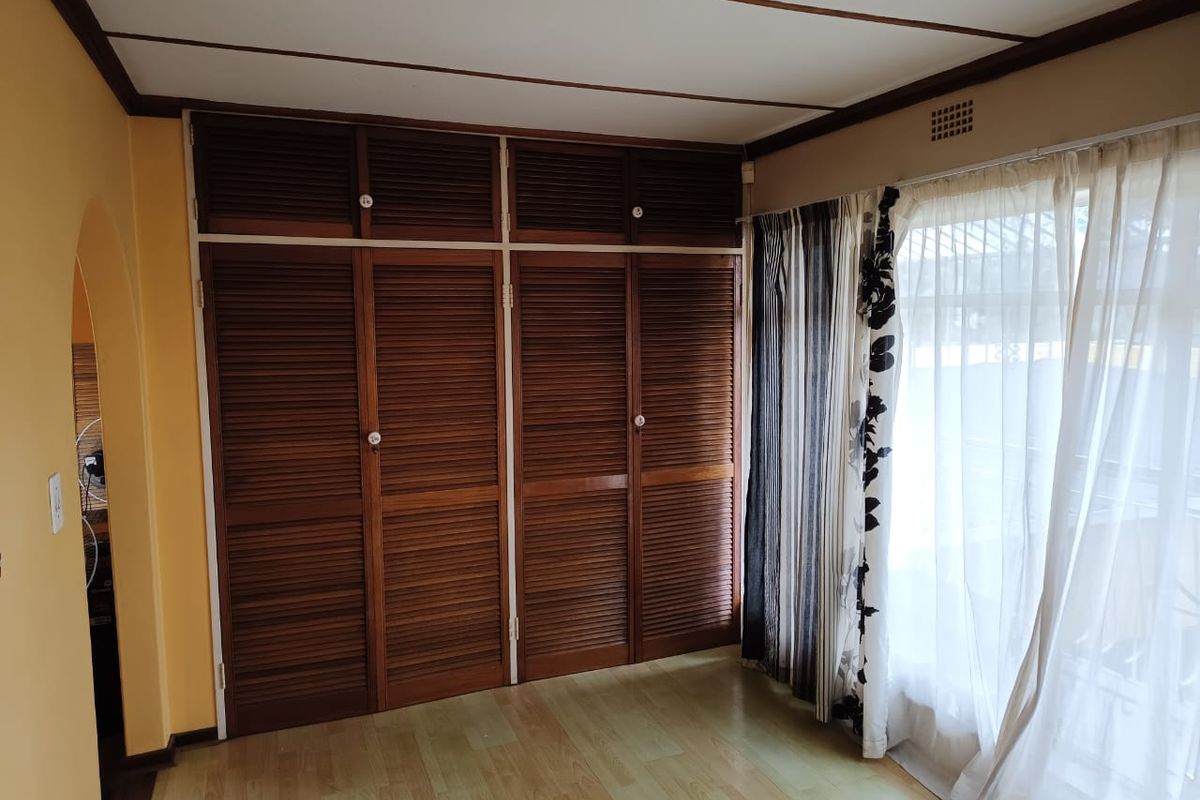 A bedroom featuring built-in wooden louvered cupboards, laminate flooring, and an arched entryway, offering a functional space ready for modernization.