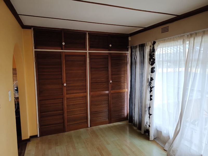 A bedroom featuring built-in wooden louvered cupboards, laminate flooring, and an arched entryway, offering a functional space ready for modernization.