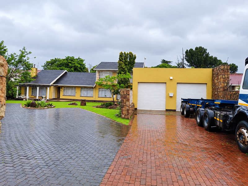 Front elevation of a well-maintained house featuring a double garage, extensive paved driveway, stone accents, and a covered patio area.
