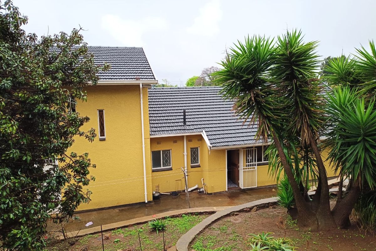 Rear view of the house featuring a tiled roof, yellow exterior walls, security gates, and a landscaped garden area with a concrete pathway.