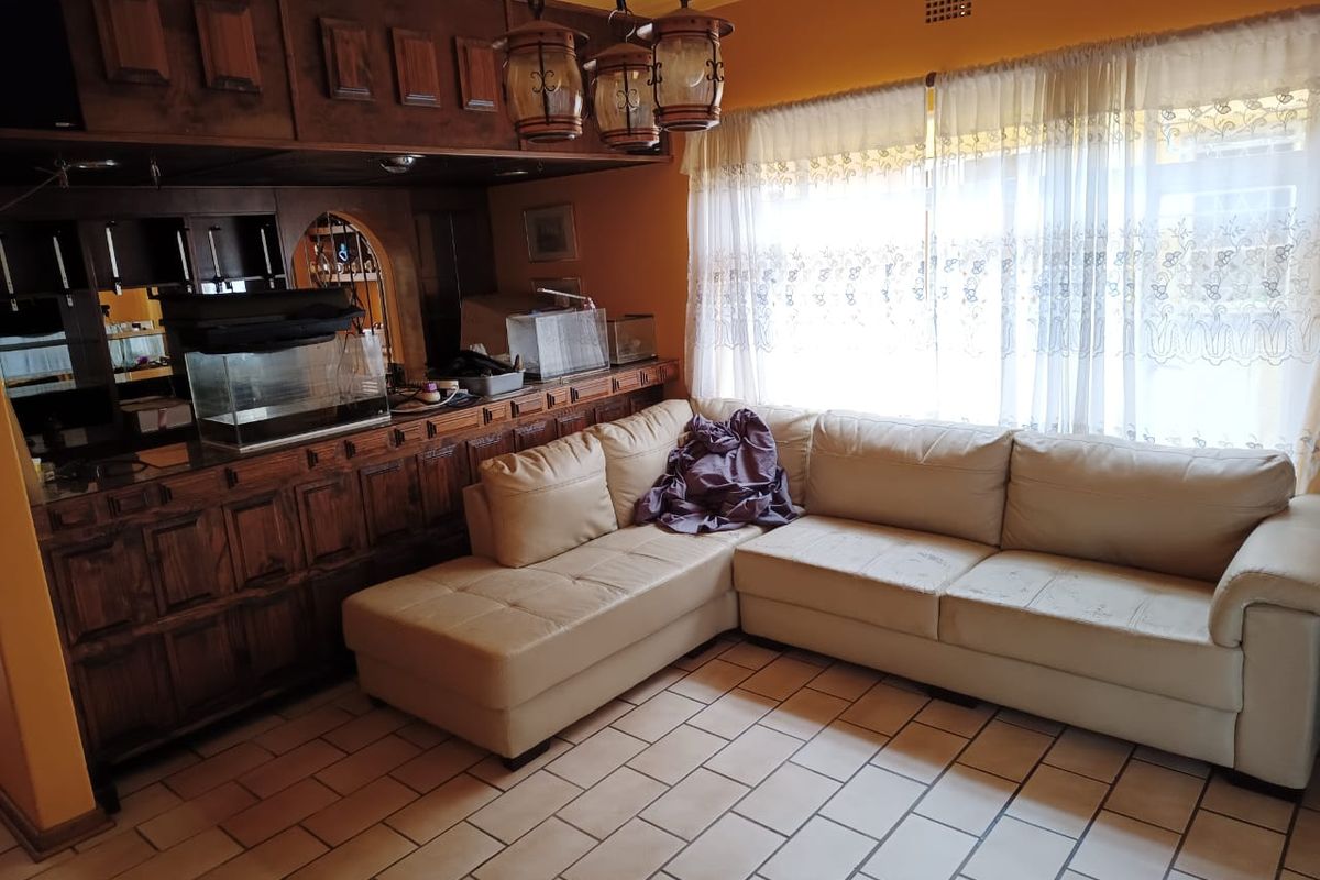A living room featuring a built-in wooden bar, tiled flooring, and a large window with natural light.