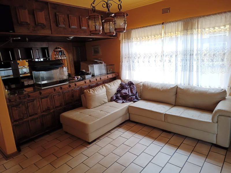 A living room featuring a built-in wooden bar, tiled flooring, and a large window with natural light.