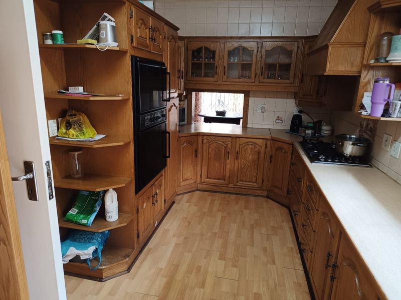 A traditional kitchen featuring extensive wooden cabinetry, built-in oven, gas hob, and tiled backsplash, offering a functional layout with ample storage space.
