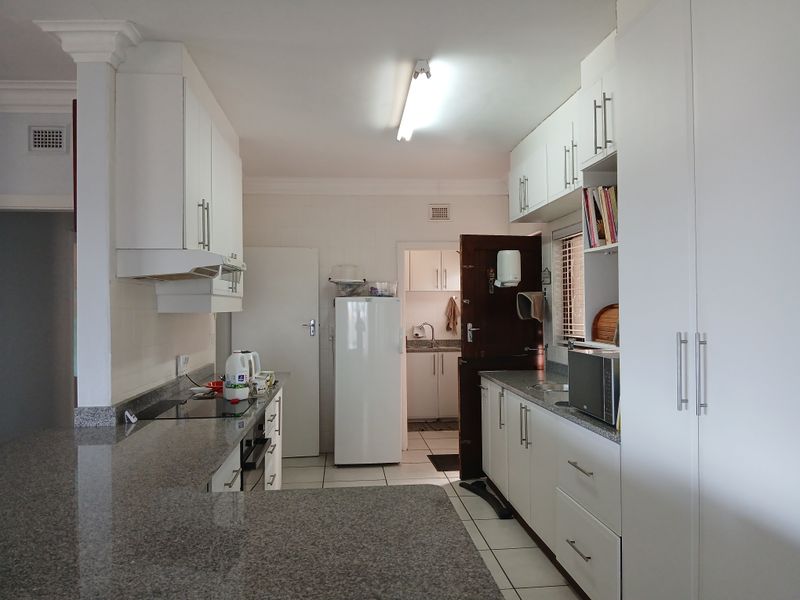 A functional kitchen featuring granite countertops, ample built-in cabinetry, an electric hob, and an integrated oven, with a connected scullery area visible.
