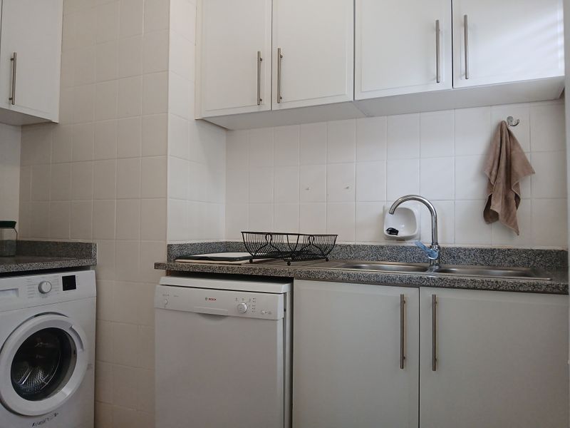 A functional laundry area featuring white cabinetry, granite countertops, a stainless steel sink, and integrated appliances including a dishwasher and washing machine.