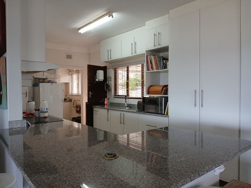 A functional kitchen featuring granite countertops, ample white cabinetry, and a breakfast bar, with an adjacent scullery area visible.