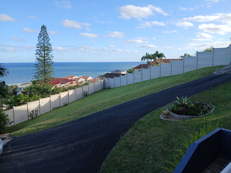 Elevated view overlooking the coastal neighbourhood and ocean, featuring a paved driveway and secure boundary walling.
