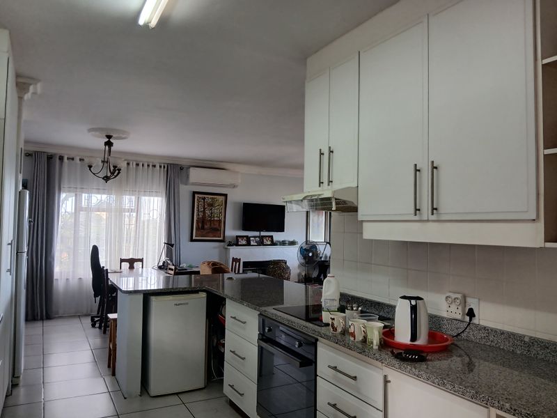 Open-plan kitchen and living area featuring white cabinetry, granite countertops, built-in appliances, and tiled flooring, creating a functional and connected living space.