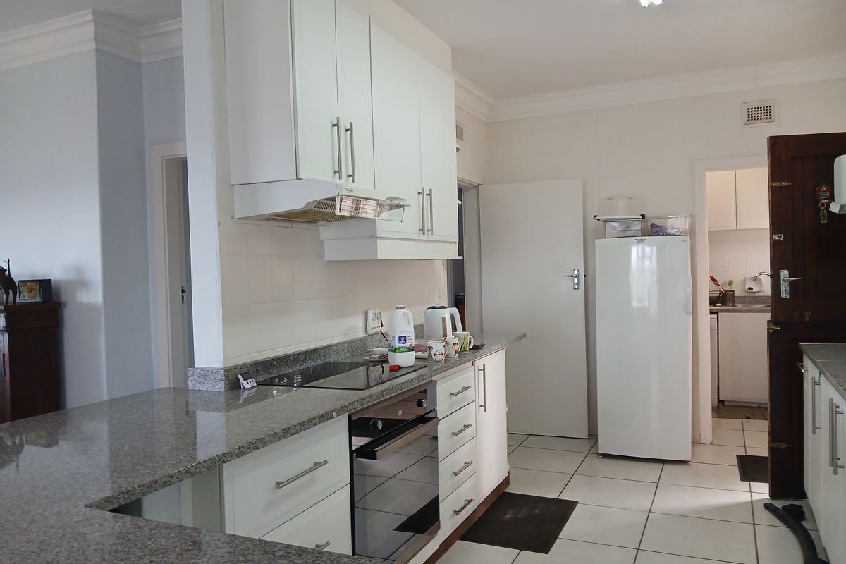 A functional kitchen featuring granite countertops, built-in cabinetry, an integrated oven and hob, and tiled flooring, with an adjacent scullery area.
