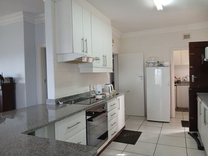 A functional kitchen featuring granite countertops, built-in cabinetry, an integrated oven and hob, and tiled flooring, with an adjacent scullery area.