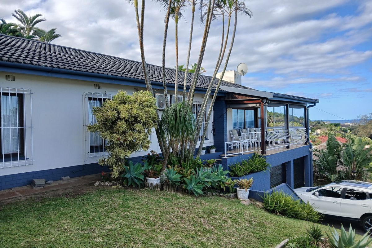 Rear elevation of the house featuring a covered patio with wrought iron railings, established garden, and integrated garage space.
