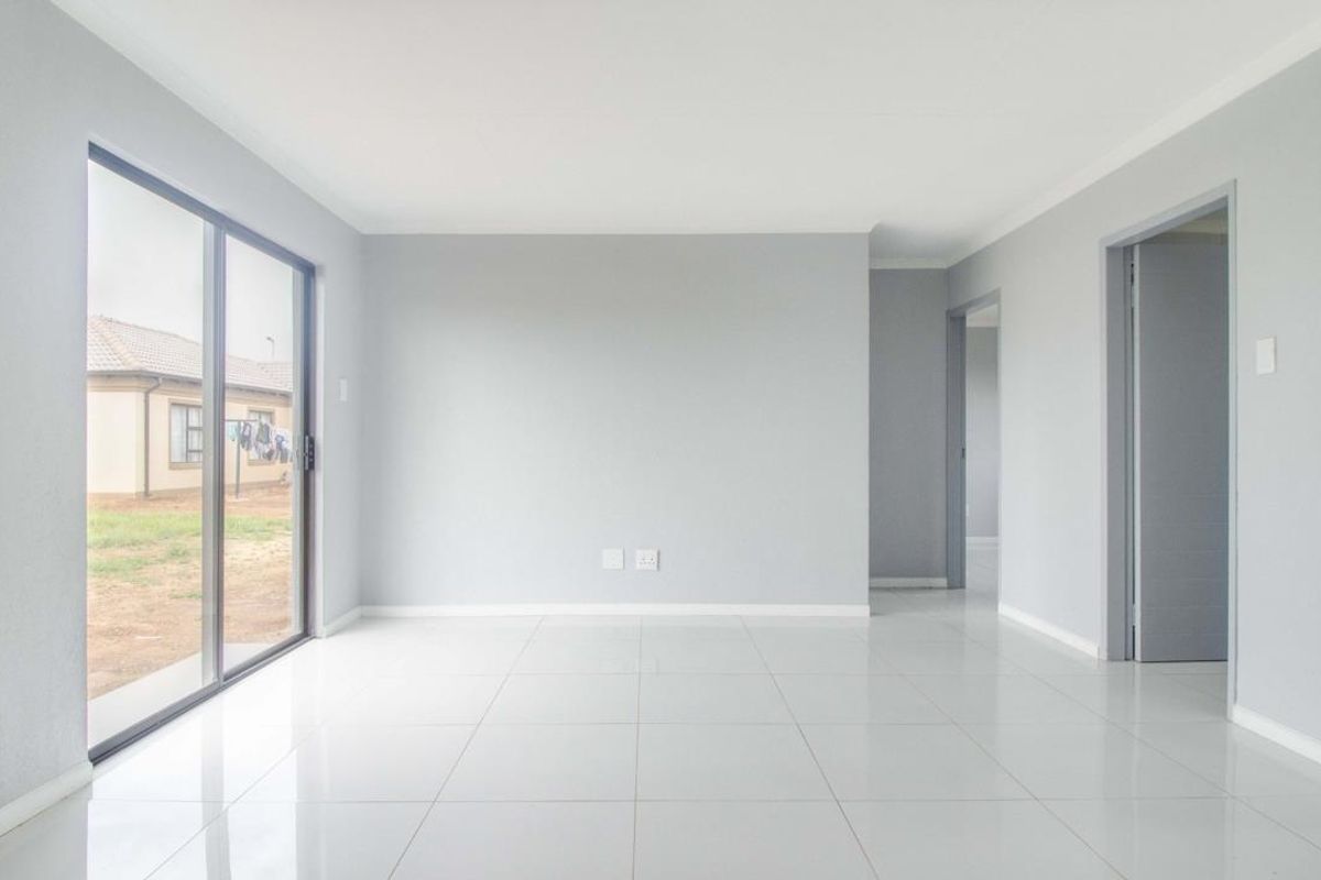 A bright, empty living room featuring neutral grey walls, polished porcelain tile flooring, and a large sliding glass door providing access to the exterior.