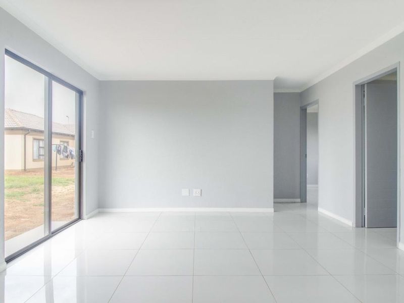 A bright, empty living room featuring neutral grey walls, polished porcelain tile flooring, and a large sliding glass door providing access to the exterior.