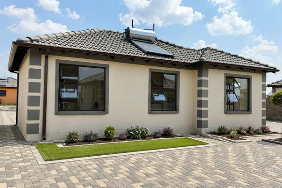 A well-maintained single-story house exterior featuring a tiled roof, solar water heating system, paved driveway, and modern aluminium window frames.