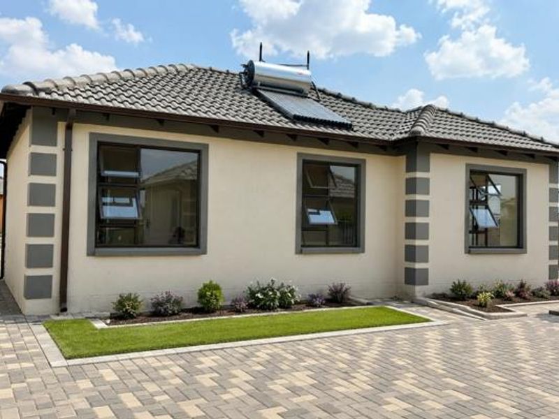 A well-maintained single-story house exterior featuring a tiled roof, solar water heating system, paved driveway, and modern aluminium window frames.