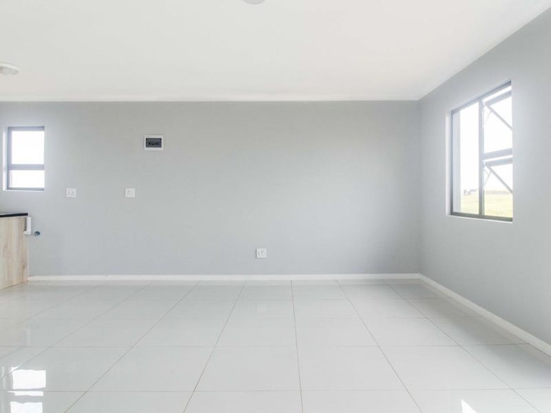 A bright, open-plan living area featuring neutral grey walls, polished white floor tiles, and a compact kitchen corner with built-in cabinetry and sink.