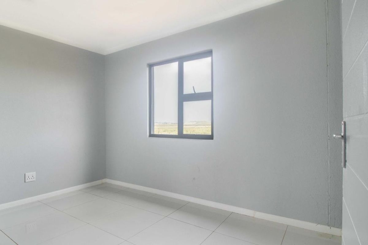 A clean, empty bedroom featuring neutral grey walls, tiled flooring, and an aluminium-framed window, providing a blank canvas for personalization.