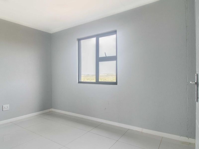 A clean, empty bedroom featuring neutral grey walls, tiled flooring, and an aluminium-framed window, providing a blank canvas for personalization.