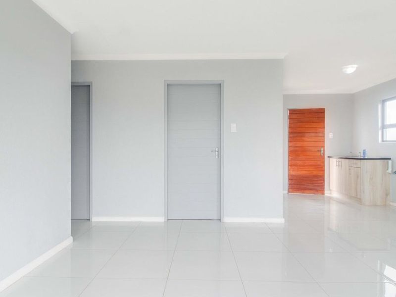 An open-plan living area featuring neutral grey walls, polished tile flooring, and a compact kitchen corner with built-in cabinetry.