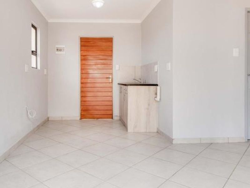 A clean, empty scullery or utility area featuring tiled flooring, a built-in sink with base cabinetry, and a wooden door.